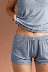 Cropped close-up shot of a slim lady in a gray-blue lingerie set made of ribbed fabric. The cosy lingerie consists of a t-shirt and shorts decorated with delicate lace and a little bow. 