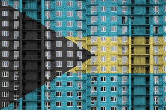 Bahamas flag depicted in paint colors on multi-storey residental building under construction. Textured banner on brick wall background