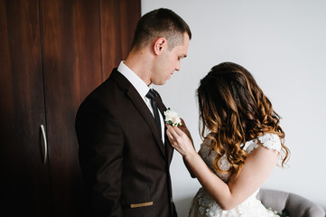 The bride in a white dress puts the groom on jacket a wedding boutonniere. Wedding concept.