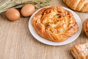 Assortment of different fresh breads, pastries, croissant, wheats and eggs over the wooden table surface.