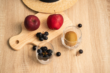 Fototapeta na wymiar Red apples and a bunch of black grapes on wooden board , a bunch of black grapes and kiwi fruit in the glass and straw hat on wooden table surface
