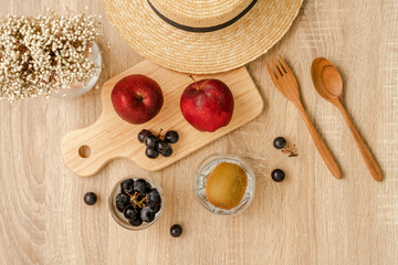 Fototapeta na wymiar Red apples and a bunch of black grapes on wooden board , a bunch of black grapes and kiwi fruit in the glass, straw hat, grass flowers and wooden spoon and fork on wooden table surface