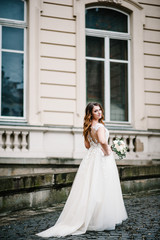 Fototapeta premium Portrait bride in wedding dress with a bouquet of flowers standing back near old building outside, vintage palace outdoor.