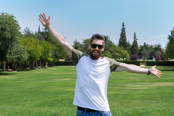 Handsome young man with a beard and sunglasses, enjoying nature, with a green and spring landscape.