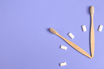 Dental care. Two wooden bamboo eco friendly toothbrushes and chewing gum in the form of hours on a purple background. Eco friendly and reuse concept. Flat lay, top view, copy space