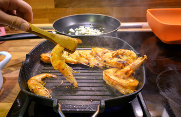 Man cooking big tiger shrimps prawns on grill pan close-up in selective focus. Grilled seafood.