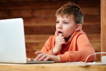 Shocked child boy with open mouth and bulging eyes looks at a computer laptop screen. Internet porn...