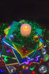 burning candle on the background of a stack of books with New Year decorations.