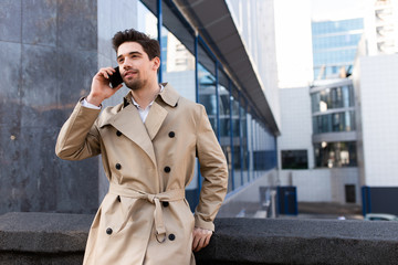 Young handsome casual man in trench coat talking on cellphone on street