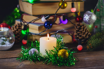 burning candle on the background of a stack of books with New Year decorations.