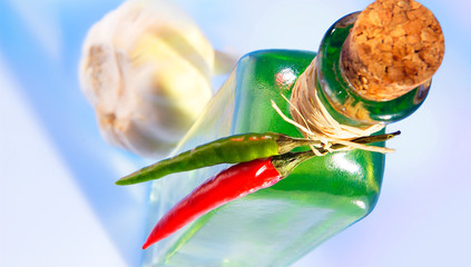 Oelflasche mit Korken und Chilischoten am Flaschenhals, im Hintergrund eine Knoblauchzehe