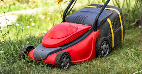 Red lawn mower with a tank for grass in green garden, backyard. Landscape, terrain concept. Closeup