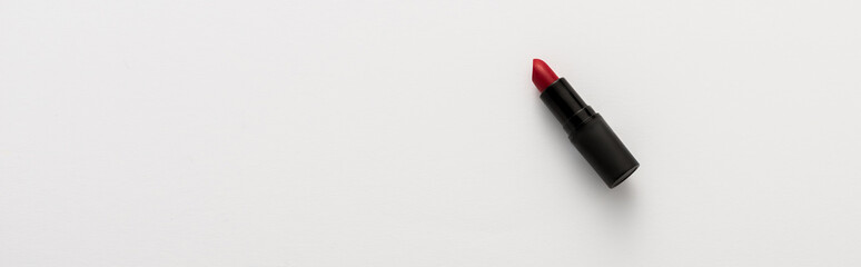 panoramic shot of black tube with red lipstick on white with copy space