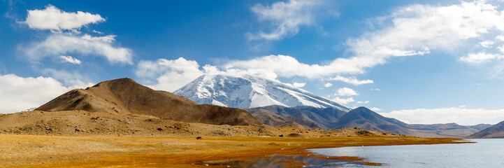 Panorama of the snow-capped Muztagh Ata mountain with Lake Karakul in the foreground. With around...
