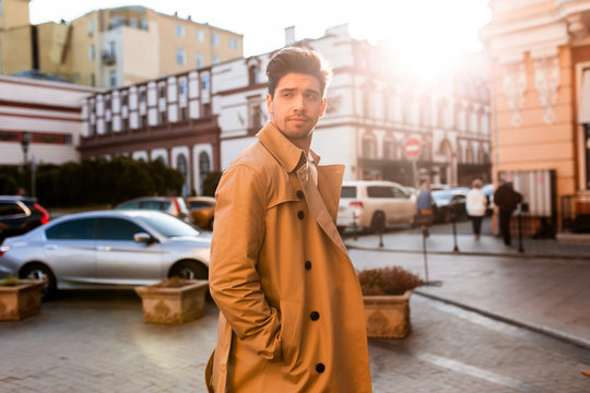 Young attractive stylish man in trench coat intently looking away on street