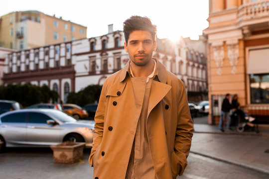 Young handsome casual man in trench coat confidently looking in camera on street