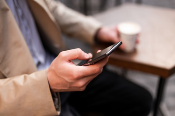 Close up casual man with coffee to go using cellphone