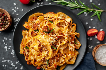 Pasta Bolognese with spices, Italian pasta dish with minced meat and tomatoes in a dark plate on a stone background