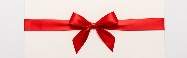 Panoramic shot of red satin bow on envelope isolated on white
