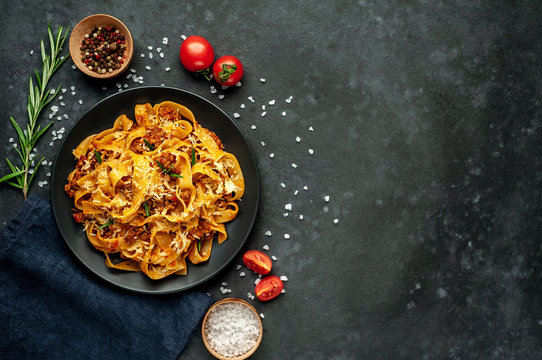 Pasta Bolognese with spices, Italian pasta dish with minced meat and tomatoes in a dark plate on a stone background with copy space for your text