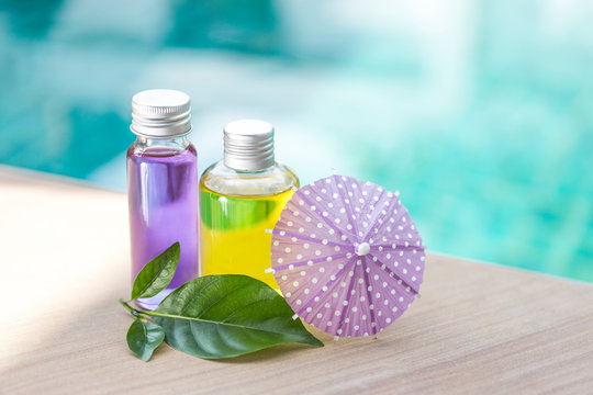 Yellow and purple gel in glass bottle with green leaf and paper umbrella over blurred blue water background, herble product concept