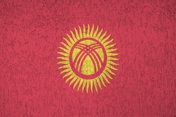 Kyrgyzstan flag depicted in bright paint colors on old relief plastering wall. Textured banner on...
