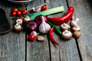 Raw vegetables  on a wooden table. Healthy nutrition. Leek, blue onion, champignons, hot pepper, sweet pepper, tomatoes