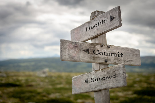 Decide commit and succeed text on wooden rustic signpost outdoors in nature/mountain scenery. Lifestyle, goals and hard work concept.