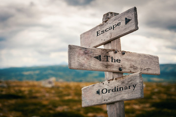 Escape the ordinary text on wooden rustic signpost outdoors in nature/mountain scenery. Adventure...