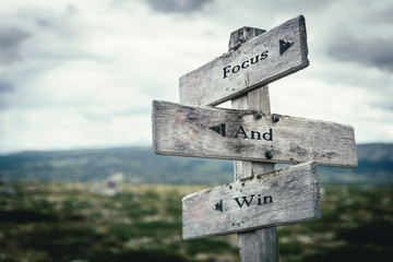 Focus and win text on wooden rustic signpost outdoors in nature/mountain scenery. Business and success concept.
