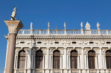 Detail of a statue on tip of a column with the Biblioteca Nazionale Marciana or national library in the background in Venice, Italy