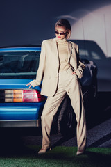 attractive and stylish woman in suit and sunglasses standing near retro car