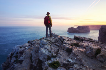 A rear view of of a lone male backpacker or hiker standing on a cliff top with an inspiring ocean...
