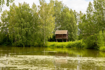 Obraz premium Rural landscape. Sheds for storage of agricultural goods are located on the river Bank among the birches. Kostroma, Russia.