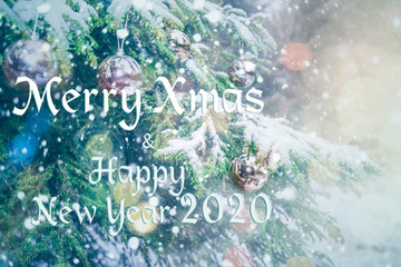 Merry Christmas and Happy New Year 2020! Blurred background of Christmas tree in snowfall decorated with silver balls, lights. Forest in snowflakes. Bokeh. Gift Greeting postcard. Wallpaper. Banner.