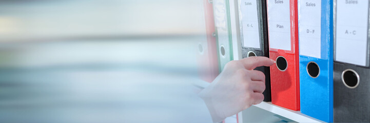 Businesswoman taking a binder from a shelf; panoramic banner