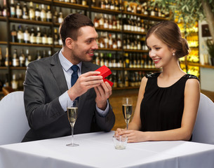 proposal, holiday and luxury concept - happy couple with gift box over restaurant or wine bar background