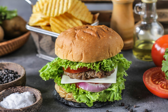 Photo of fresh burger on wooden cutting board on dark background..Homemade hamburger with beef, onion, tomato, lettuce and cheese. Homemade fast food. Dark textured background. Copy space. Image.
