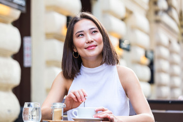 Beautiful Asian young woman with cup of coffee. Woman enjoys fresh coffee in the morning with sunrise at coffe shop Beautiful woman drinking coffee in the morning sitting outdoors