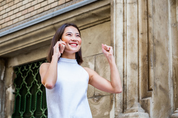 Asian cheerful young woman walking along the street and talking on phone. Asian happy woman walking on the street, wearing cute trendy outfit and talking om her smart phone.