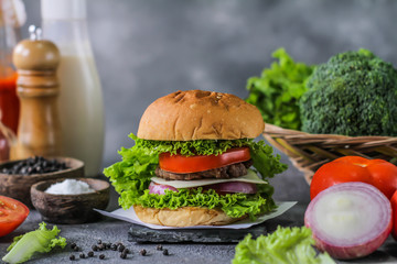 Photo of fresh burger on wooden cutting board on dark background..Homemade hamburger with beef, onion, tomato, lettuce and cheese. Homemade fast food. Dark textured background. Copy space. Image.