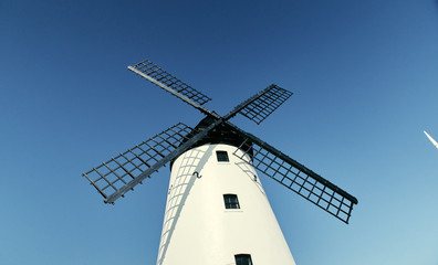 A vintage dutch style windmill against a beautiful blue clear sky. Windmills produce a clean way of harnessing the earths natural power resource of wind. Clean energy in farming and food production.