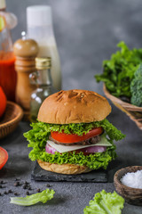 Photo of fresh burger on wooden cutting board on dark background..Homemade hamburger with beef, onion, tomato, lettuce and cheese. Homemade fast food. Dark textured background. Copy space. Image.