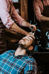 tattooed hairdresser washing hair of man in black sink near mirror