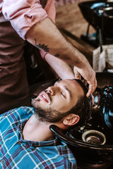 tattooed barber washing hair of handsome man with closed eyes