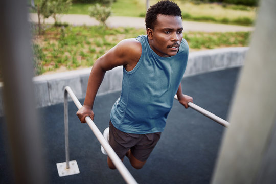 Young african american fit man doing triceps dips on parallel bars at an outdoor gym park