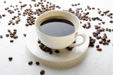 Closeup of white porcelain cup of black coffee on the saucer, coffee beans on the white surface