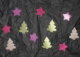 Shiny Christmas trees and stars on a dark crumpled background.