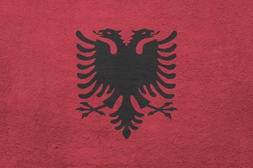 Albania flag depicted in bright paint colors on old relief plastering wall. Textured banner on...