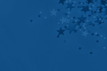 Metallic foil stars confetti sparse on trendy classic blue background. Simple holiday concept. Design template. Corner frame with copy space for text. Top view, flat lay. Color of the year 20